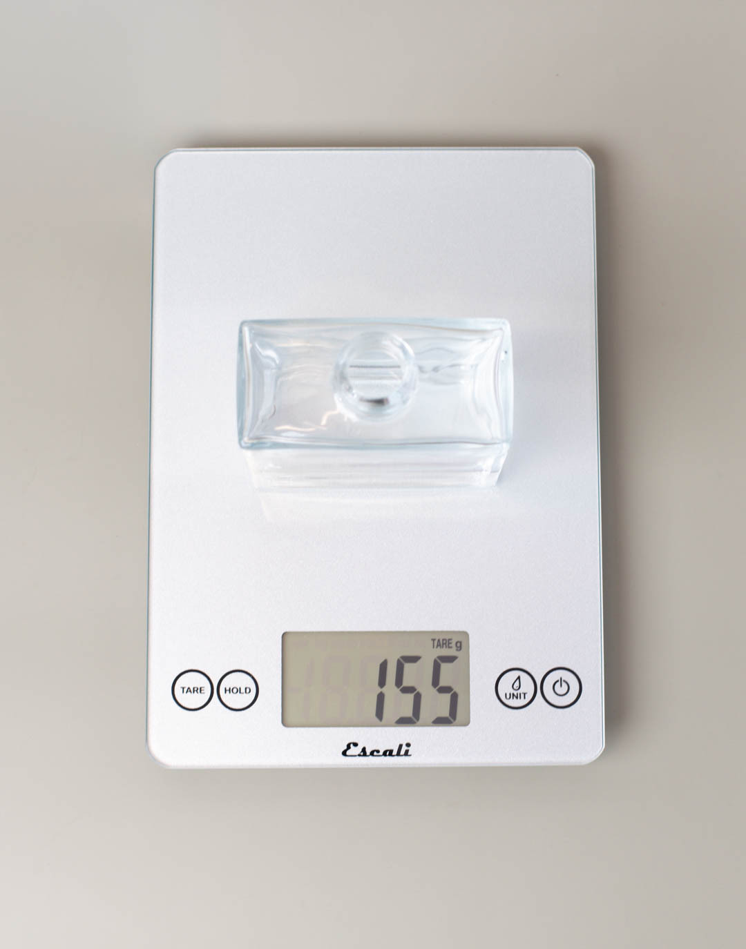 An empty glass reed diffuser on a scale, the weight is 155 g.